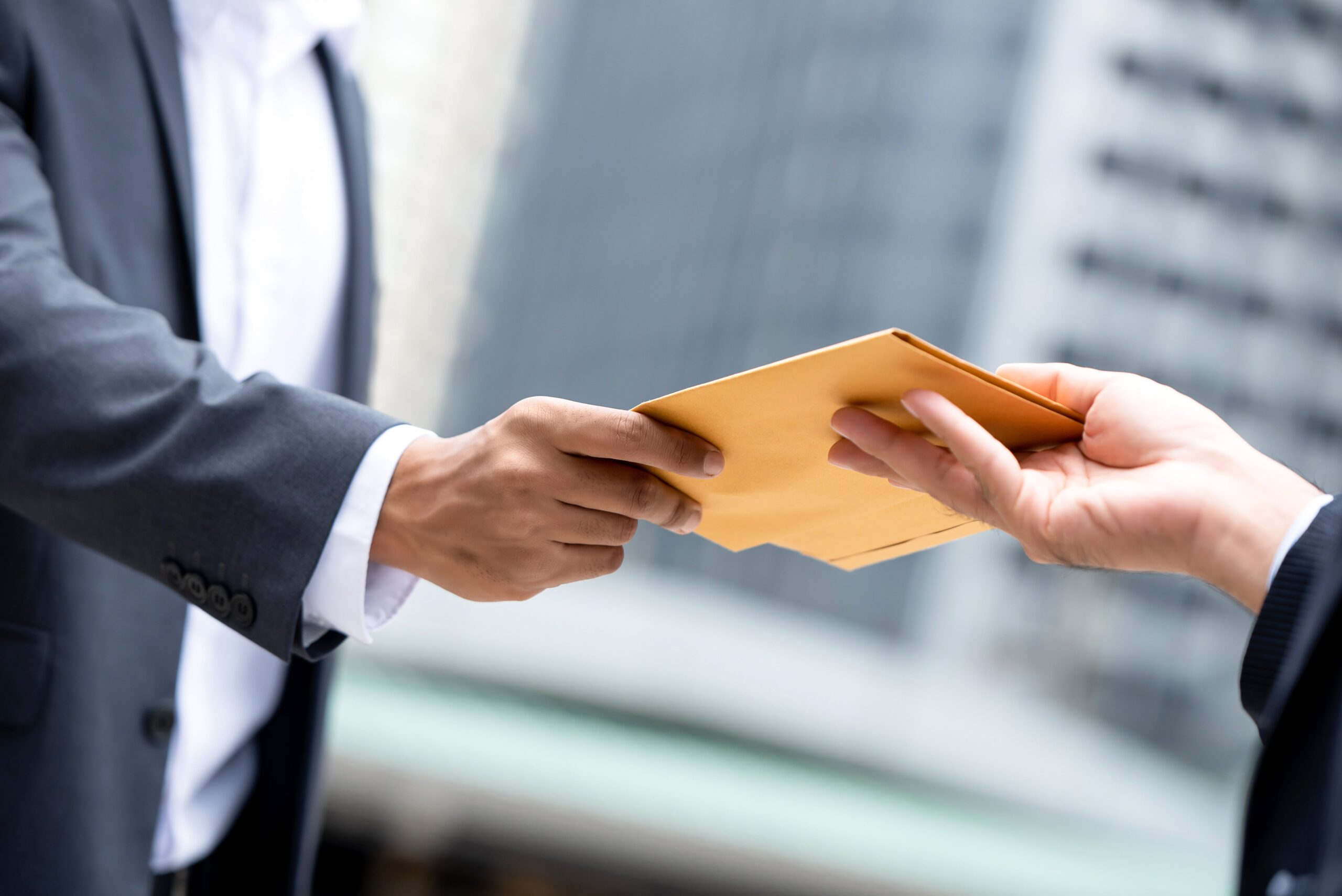 close up portrait businessman hand recieving yellow envelope from boss urban city background min scaled
